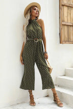 Woman wearing a green polka dot halter neck wide leg jumpsuit with a belt and straw hat.