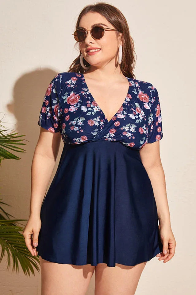 Plus-size woman wearing a navy blue floral print one-piece swimsuit with short sleeves and a skirted bottom.