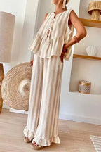 Woman wearing a beige and white striped sleeveless tiered top with tie-front closure and wide leg pants with ruffled hems.