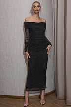 Woman wearing a black off-the-shoulder floor-length dress with sparkling embellishments, standing against a neutral backdrop.