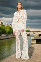 Woman wearing a sheer white lace button-down shirt and flare leg pants standing by a river in Paris.