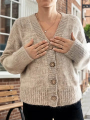 Woman touching her chest while wearing a beige button-up cardigan.