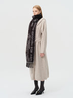 Side profile of a woman wearing a beige cardigan and a black scarf with white text