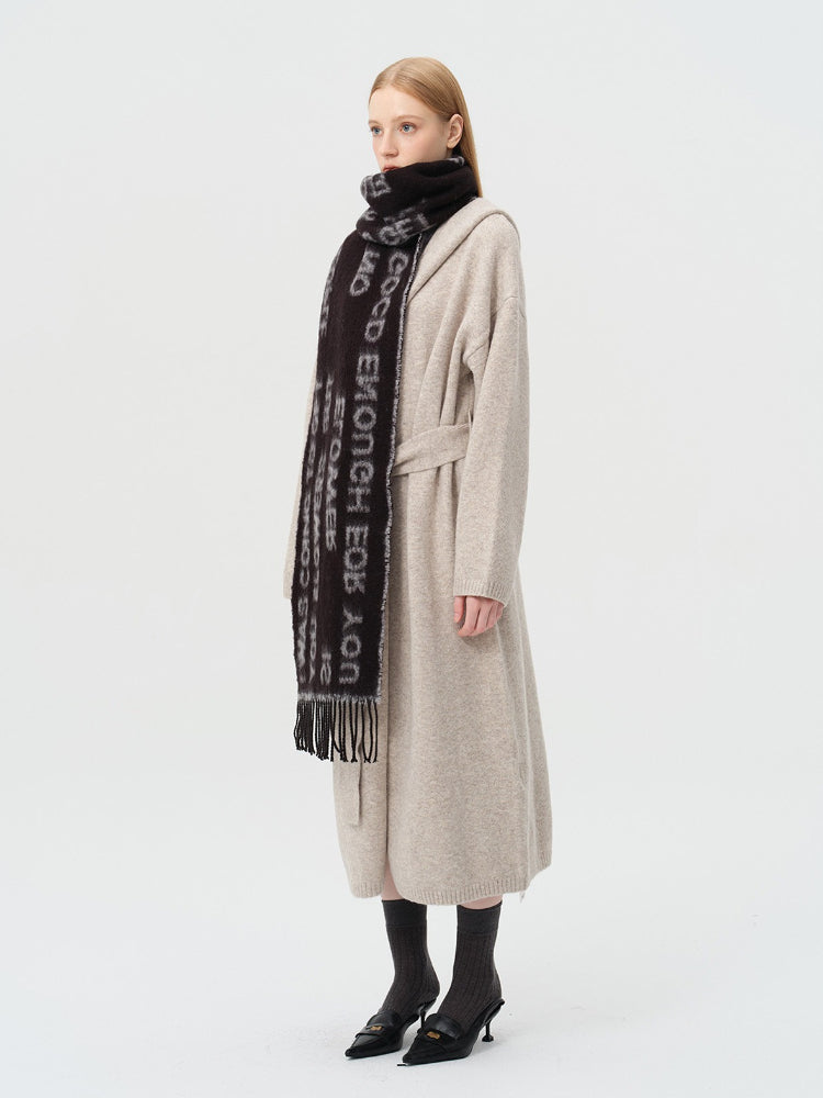 Side profile of a woman wearing a beige cardigan and a black scarf with white text