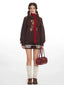 Woman wearing a brown knit sweater with a teddy bear graphic and a red scarf, paired with a patterned skirt and leg warmers