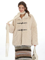 Close-up of a woman wearing a cream-colored fleece coat with toggle closures and a cream scarf, smiling.