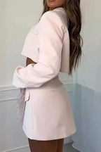 Back view of a woman wearing a pink cropped blazer and asymmetrical skirt with feather trim