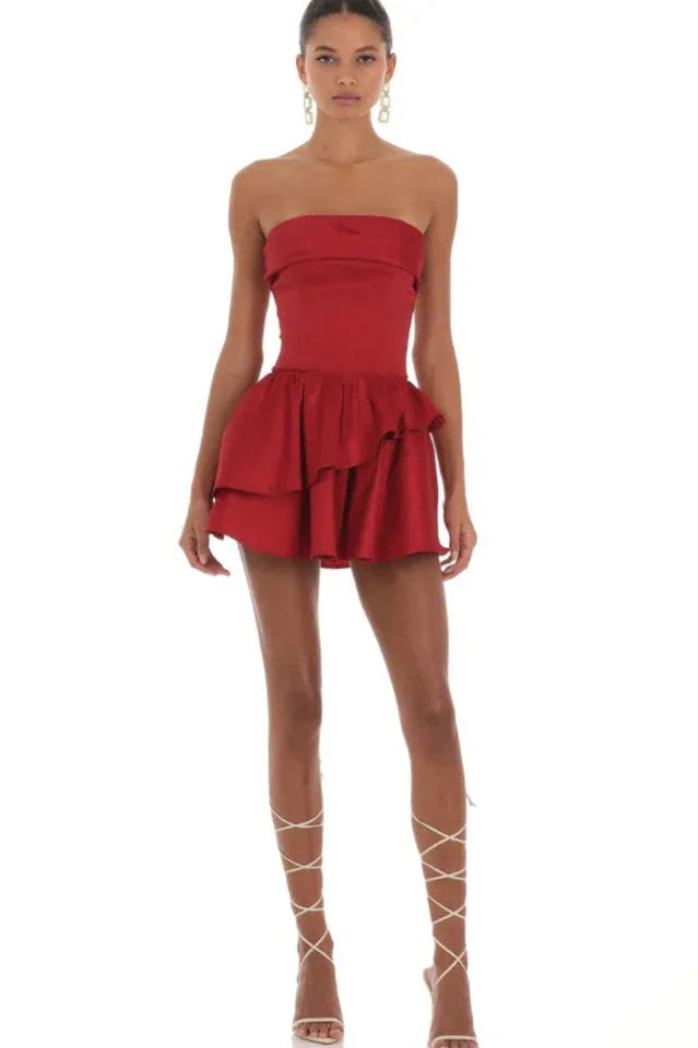 Full-length view of a woman in a red strapless mini dress with a tiered ruffled skirt and lace-up back detail. Secondary image