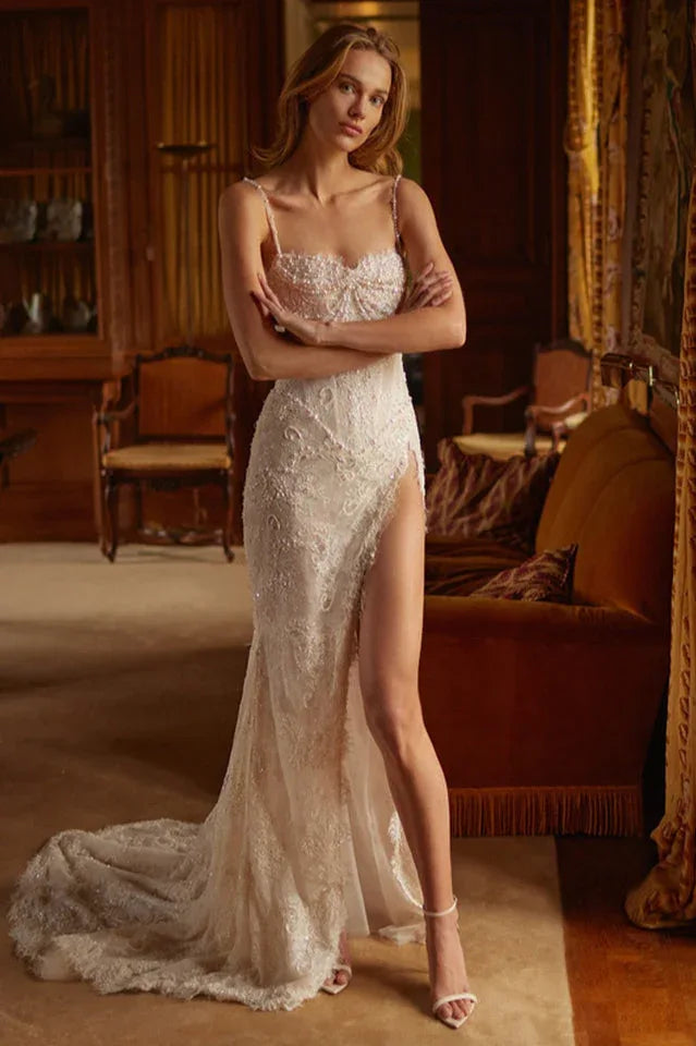 A woman in a white, beaded mermaid wedding dress with a high slit and train, standing with her arms crossed. Main image