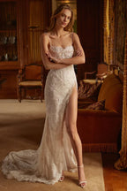 A woman in a white, beaded mermaid wedding dress with a high slit and train, standing with her arms crossed.