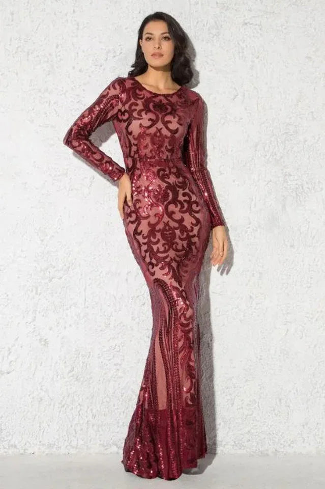 Woman in a long-sleeved, floor-length red sequined dress with a burnout pattern, standing against a textured wall. Main image
