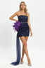Woman wearing a navy blue strapless sequined mini dress with purple feather and navy blue tulle detailing on the hip and a flowing train, posing against a white background.