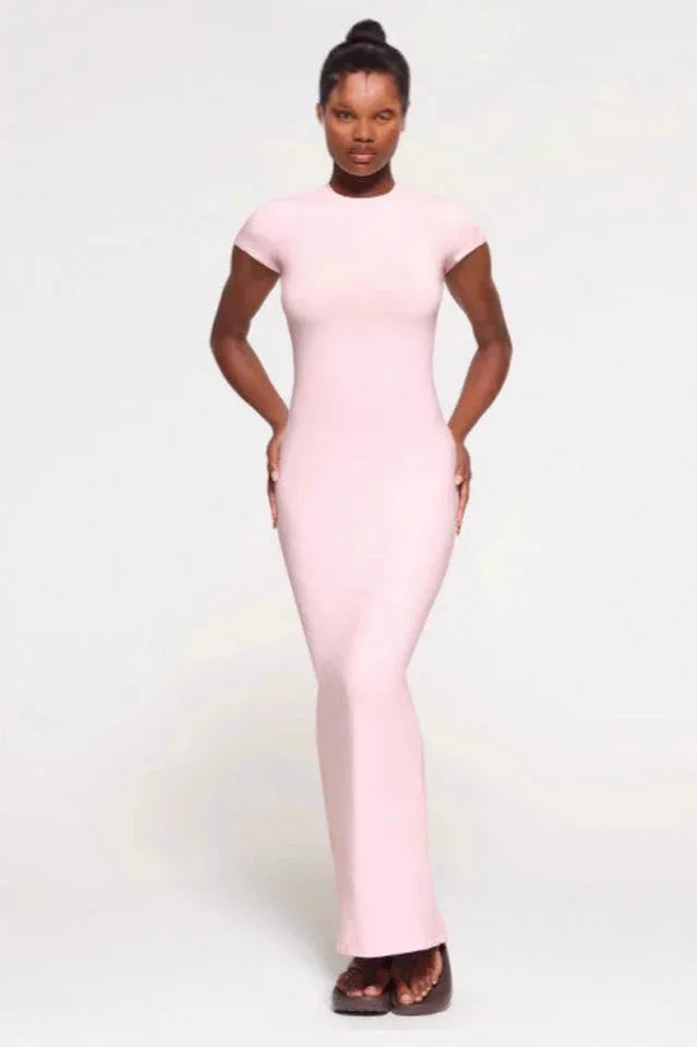 Woman wearing a light pink full-length ribbed knit dress with short sleeves and a crew neck, standing with hands on hips against a white background. Main image