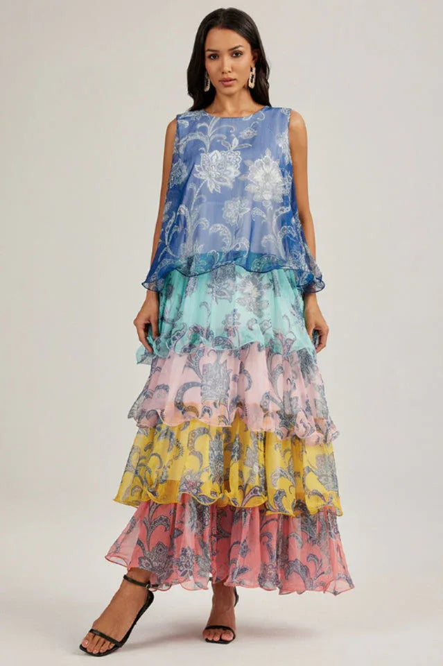 Woman wearing a blue, teal, pink, yellow, and pink tiered maxi dress with a floral print and ruffled hem. Main image