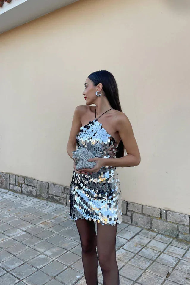 Woman in a silver sequined halter mini dress, black tights, and holding a beaded clutch.