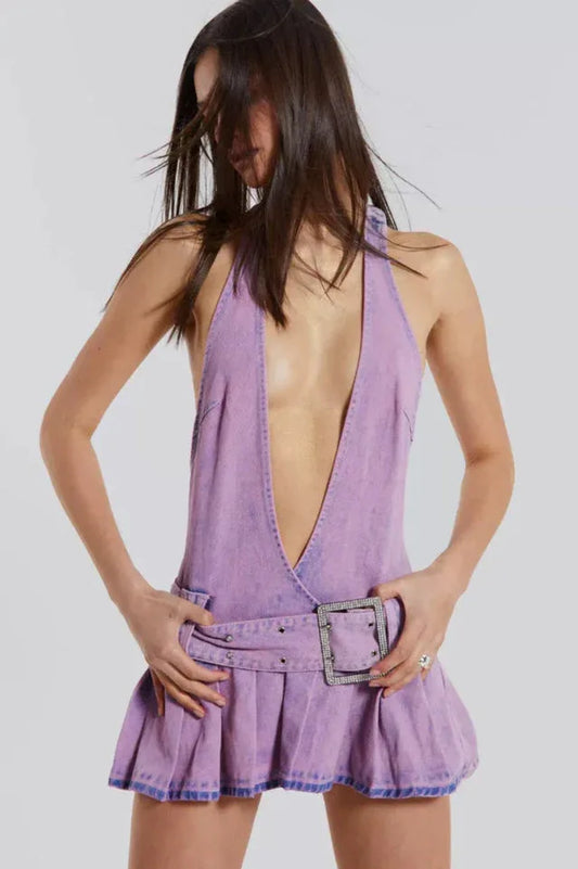 Woman in a lavender denim halter mini dress with a plunging neckline and a pleated skirt, hands on hips.