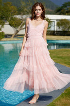 Woman wearing a light pink tiered tulle dress with thin straps and a v-neckline, standing by a pool.