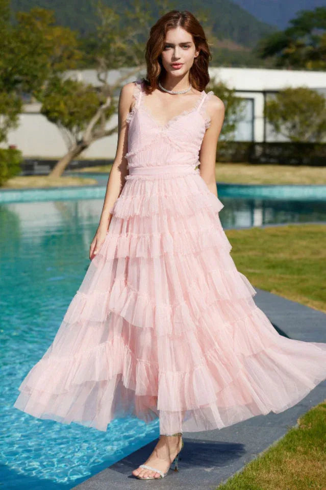 Woman wearing a light pink tiered tulle dress with thin straps and a v-neckline, standing by a pool.