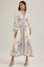 Woman wearing a long, cream-colored maxi dress with a blue peacock print and long sleeves.