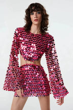 Front view of a woman wearing a pink sequined crop top with bell sleeves and a matching mini skirt with a cut-out detail at the waist.