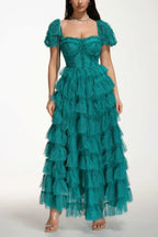 Woman wearing a floor-length emerald green tiered tulle gown with puff sleeves and a sweetheart neckline.