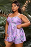 Plus-size woman wearing a purple floral print tankini with shorts, standing in front of tropical foliage.