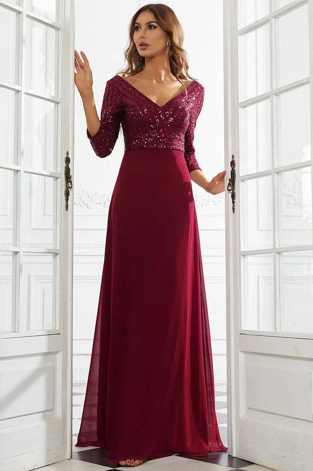 Woman wearing a floor-length burgundy sequined formal gown with 3/4 sleeves, standing in a doorway.
