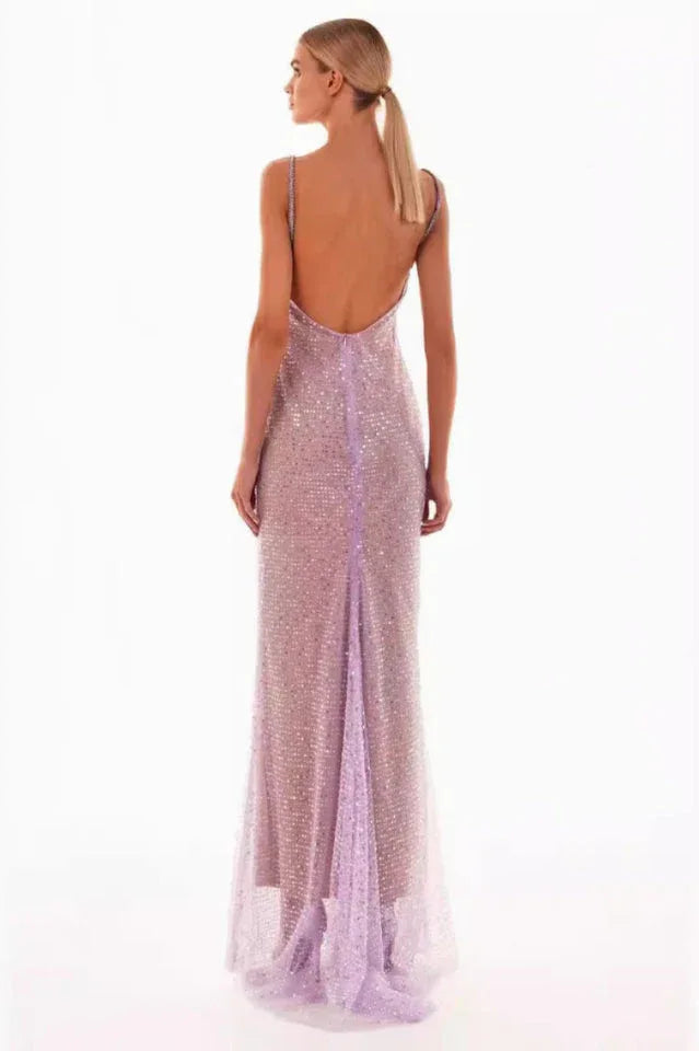 A woman models a sparkling lavender floor-length gown with a cowl neckline and spaghetti straps, back view.