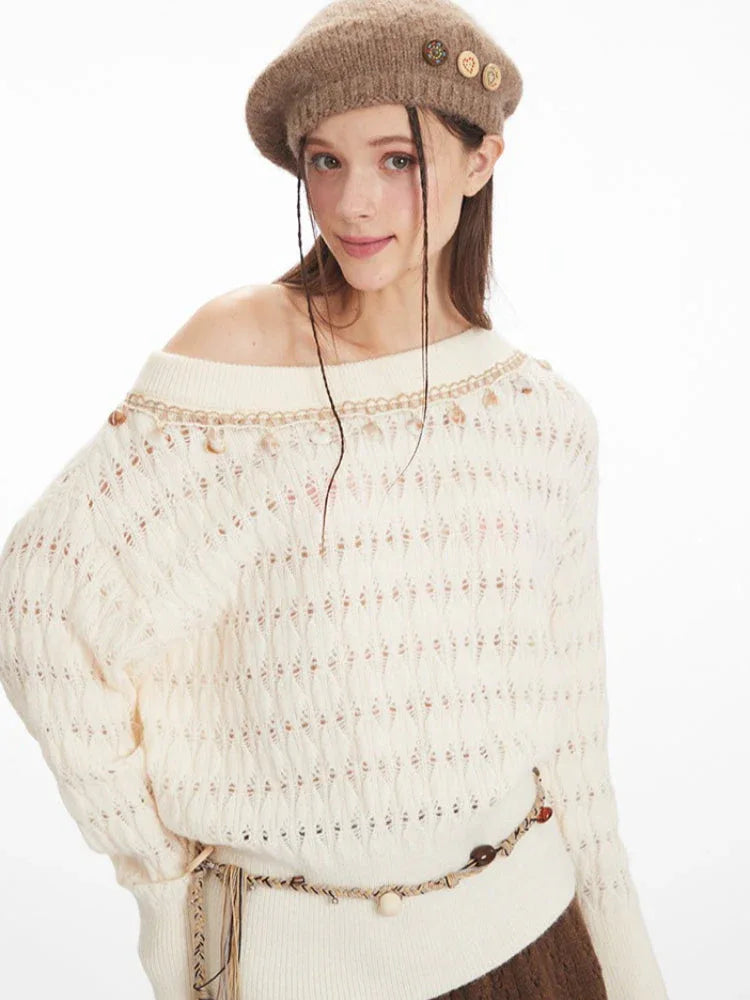 Detailed view of the neckline and embellishments on the cream-colored off-the-shoulder knit sweater.