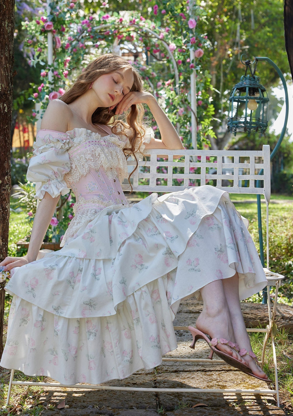 Model posing in a garden wearing a white floral print off-the-shoulder tiered dress
