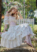 Model posing in a garden wearing a white floral print off-the-shoulder tiered dress