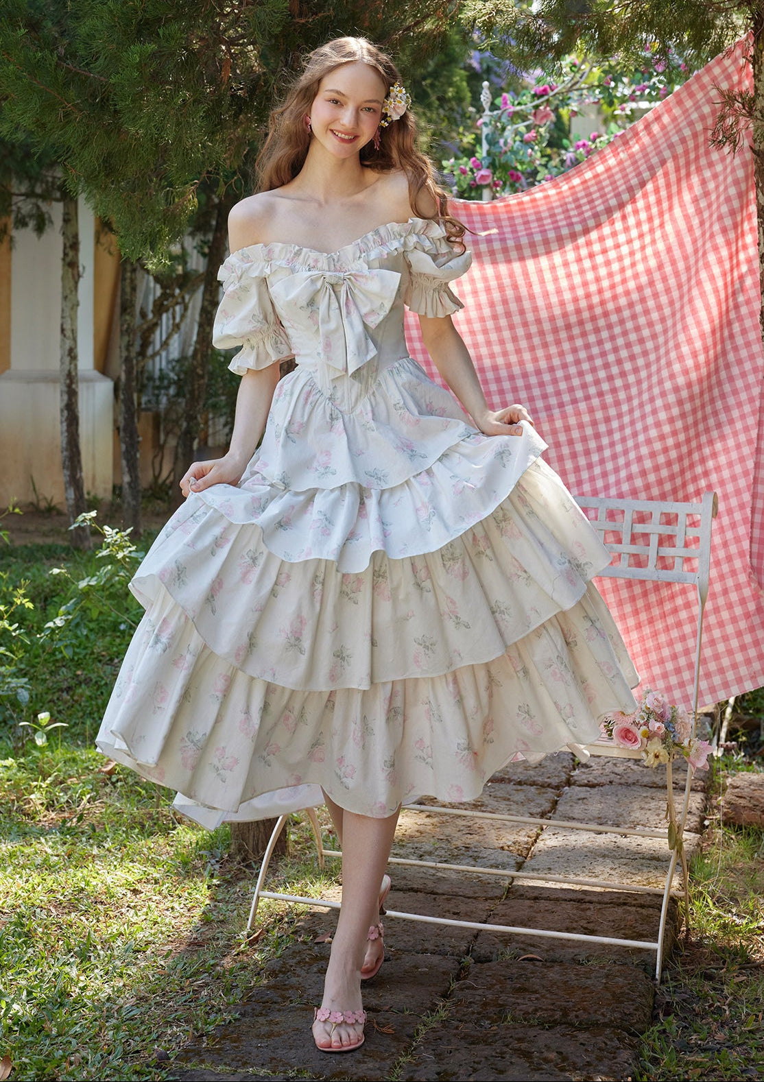 Woman wearing a white floral print off-the-shoulder tiered dress with puffed sleeves and a bow detail