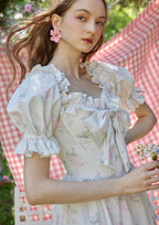 Flat lay of a white floral print off-the-shoulder tiered dress with puffed sleeves and a bow detail