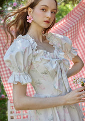 Flat lay of a white floral print off-the-shoulder tiered dress with puffed sleeves and a bow detail