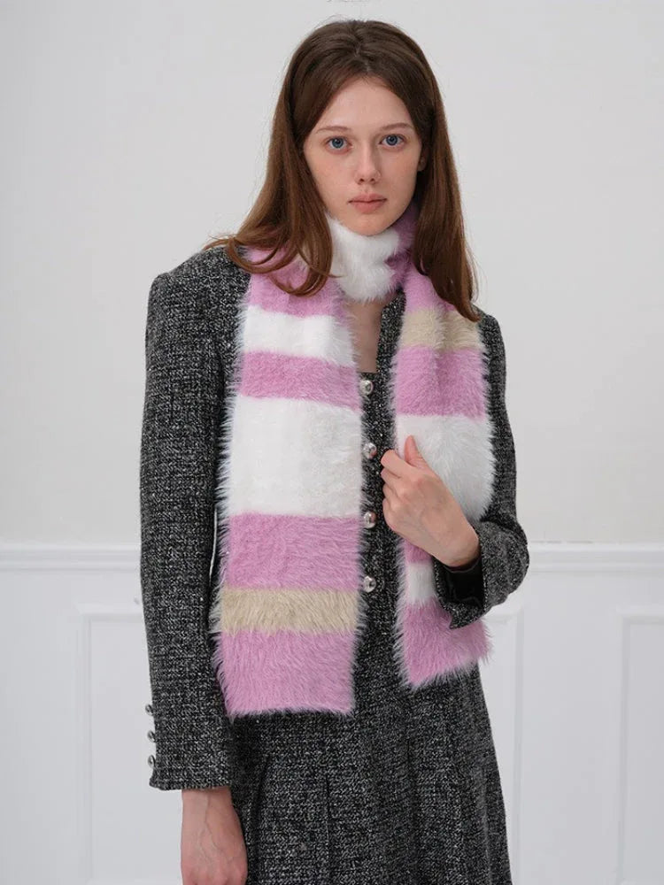 Woman wearing a pink, white, and beige striped fuzzy scarf with her hand on the scarf.