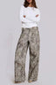 Model wearing wide leg leopard print denim pants and a white long-sleeved shirt, arms crossed.