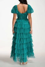 Back view of a woman in a floor-length emerald green tiered tulle gown with puff sleeves.