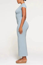 Side view of a woman wearing a light blue full-length ribbed knit dress with short sleeves and a crew neck, highlighting the fitted silhouette and side slit.