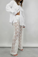 Side view of a woman adjusting her white oversized button-down shirt to show her white lace wide-leg pants.