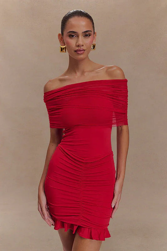 Model wearing a red off-the-shoulder ruched dress with a sheer overlay and ruffled hem.