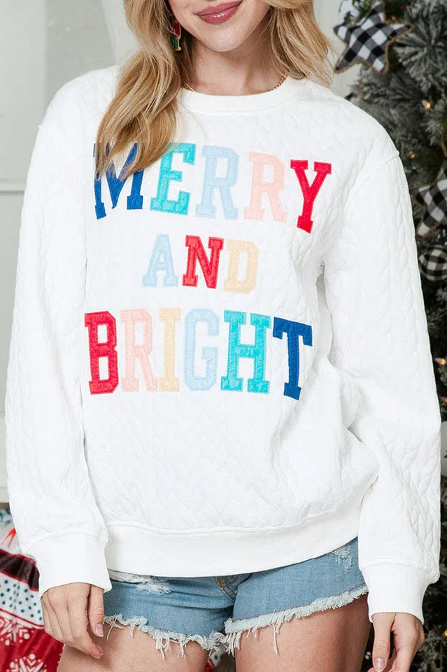 Close-up of the "MERRY AND BRIGHT" embroidery on a white quilted crewneck sweatshirt.