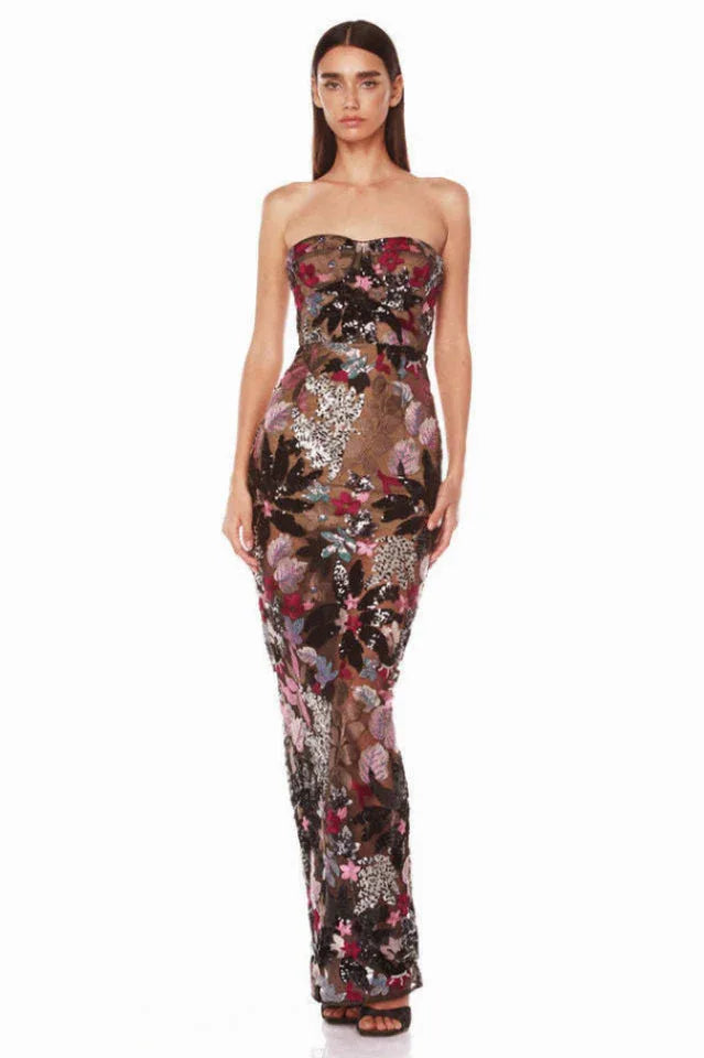 Woman wearing a strapless, floor-length column dress with a sweetheart neckline. The dress is adorned with vibrant floral embroidery and shimmering sequins on a sheer black base. Main image