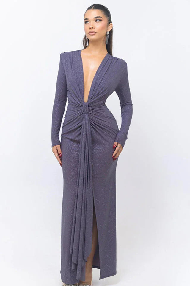 Woman wearing a long, dark purple, sparkly dress with a deep V-neck and long sleeves, standing against a white background. Main image