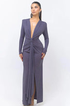 Woman wearing a long, dark purple, sparkly dress with a deep V-neck and long sleeves, standing against a white background.