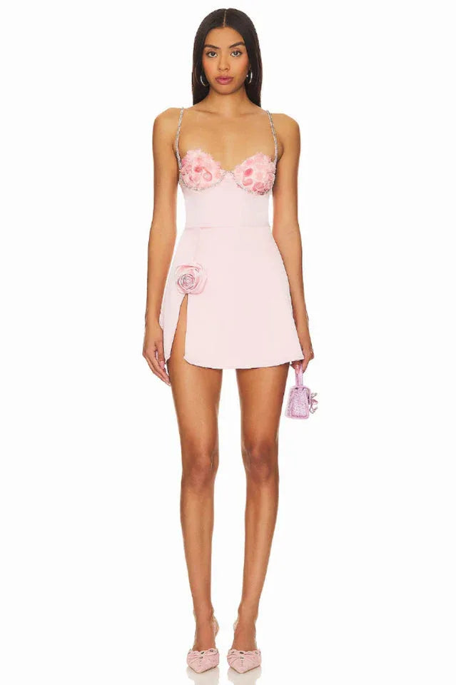 A full-body shot of a woman wearing a pink mini dress with floral details and a small handbag. Secondary image