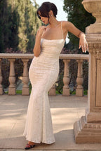 Woman wearing a white lace mermaid wedding dress with spaghetti straps and a low back, leaning against a stone pillar.