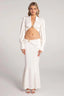 Woman wearing a white satin two-piece set consisting of a cropped long-sleeved top and a floor-length mermaid skirt.