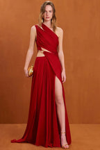 Woman wearing a red one-shoulder draped chiffon gown with a high slit and gold ring detail, holding a gold clutch.
