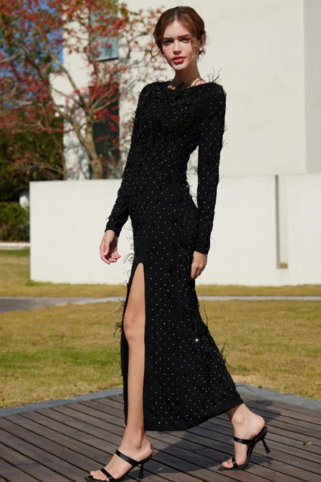Woman wearing a black sparkly maxi dress with a high slit and feather trim, posing outdoors.