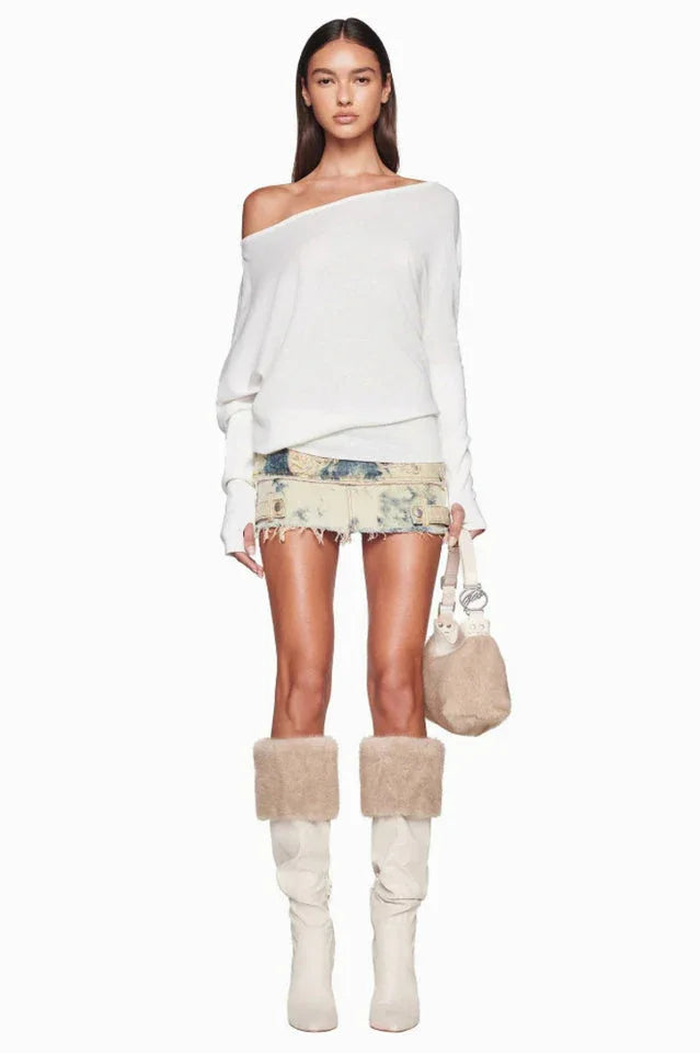 Woman wearing a white off-the-shoulder sweater and a distressed denim mini skirt, with cream boots and fur trim, holding a small beige handbag. Main image